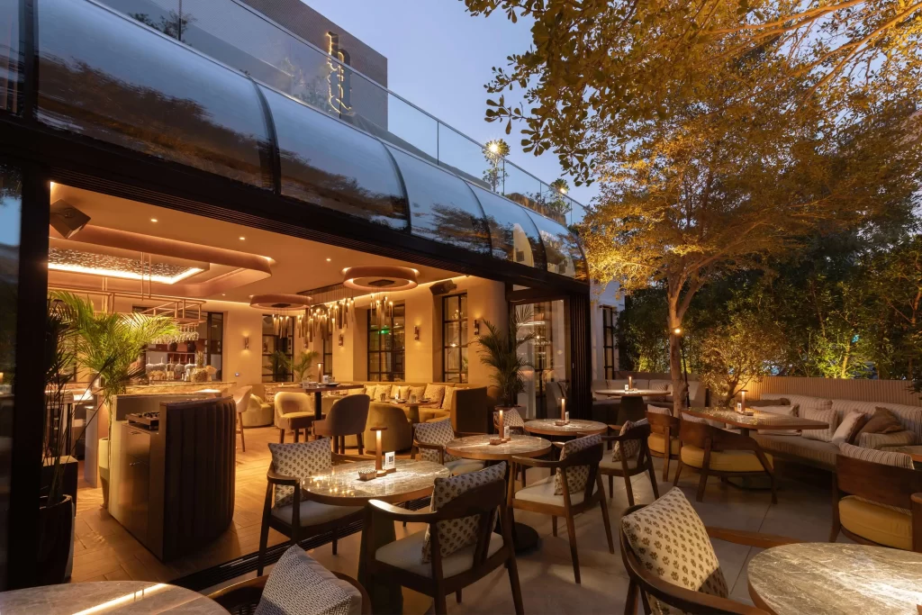 candlelit outdoor terrace with marble tables, wood chairs, and mature trees at dusk