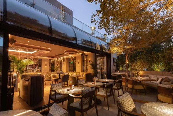 candlelit outdoor terrace with marble tables, wood chairs, and mature trees at dusk