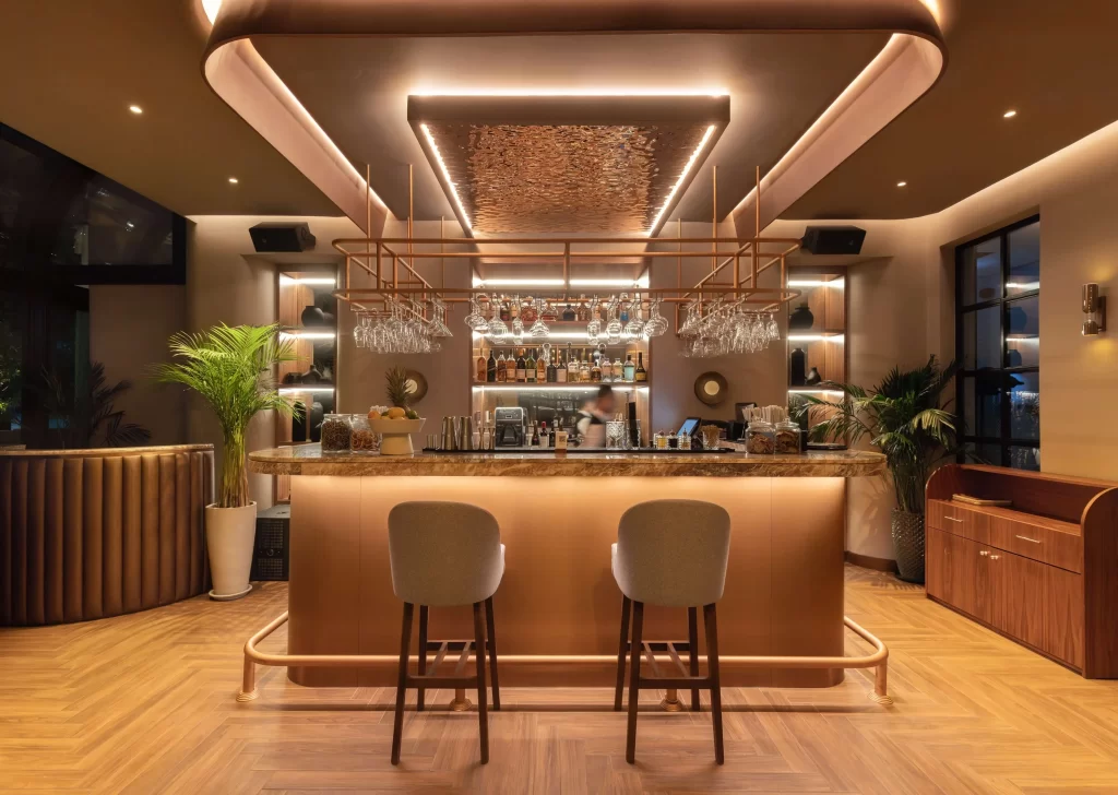 HAUS (9) urved copper bar counter with backlit shelving, hanging glassware, and rippled metal ceiling feature